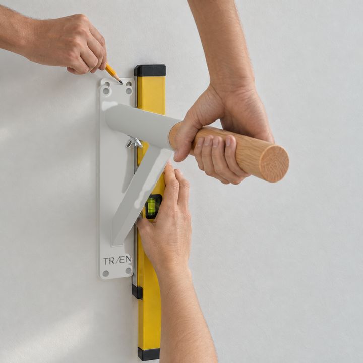Eine Platte wird senkrecht an die Wand gehalten; ein Stift zeichnet die Löcher an.