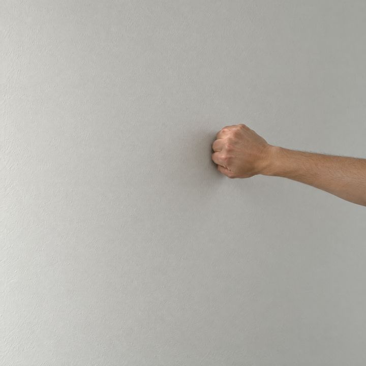 Eine Faust klopft an eine freie Wand auf Brusthöhe.