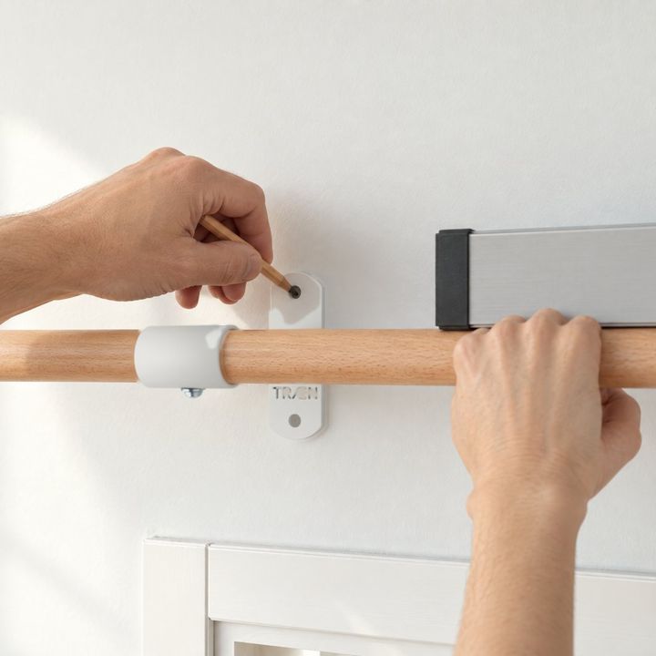 Zwei Hände halten die vormontierte Stange über dem Türrahmen an die Wand und zeichnen die Löcher an.