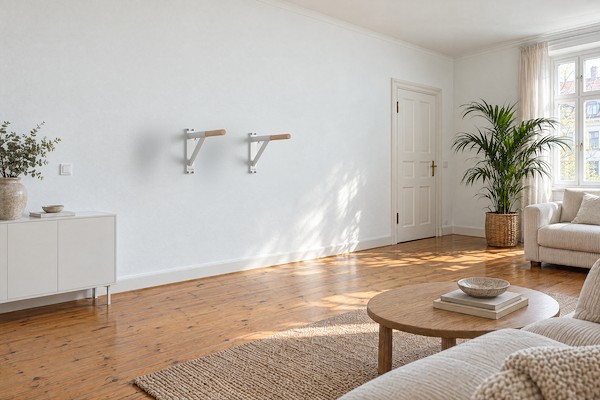 Zwei weiße Dip-Barren-Griffe DB1 mit Buche an der Wand eines hellen Altbau-Wohnzimmers mit Dielenboden, Sofa und Couchtisch.